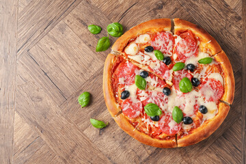 Tasty pizza with salami, cheese, basil and olives on wooden table, flat lay. Space for text