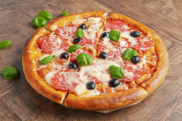 Tasty pizza with salami, cheese, basil and olives on wooden table, closeup