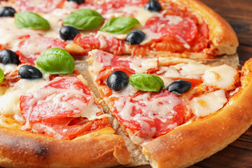 Tasty pizza with salami, cheese, basil and olives on table, closeup