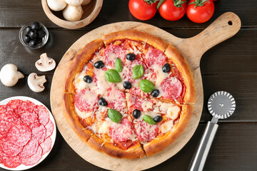 Tasty pizza, ingredients and cutter on black wooden table, flat lay