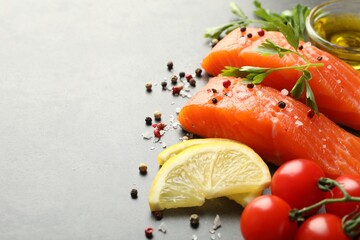 Seafood. Pieces of salmon fillet, spices, lemon slices and oil on gray table, closeup, Space for text