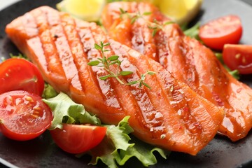 Tasty grilled salmon served with lettuce, tomatoes and lemon on table, closeup