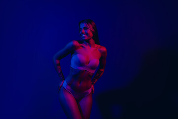 Obraz premium Fashionable young woman posing in neon light, showcasing style and confidence, with a vibrant and glowing blue background