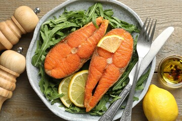 Seafood. Tasty salmon steaks served with arugula and lemon on wooden table, flat lay