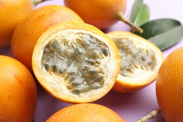 Ripe yellow passion fruits and leaves on lilac background, closeup