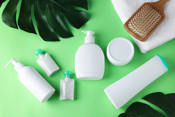Different bath accessories and monstera leaves on green background, flat lay