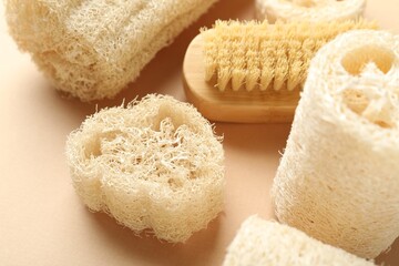 Natural loofah sponges and brush on beige background, closeup