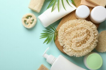 Natural loofah sponges, cosmetic products and green twigs on light blue background, flat lay. Space for text