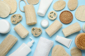 Natural loofah sponges, cosmetic products, towel and brush on light blue background, flat lay