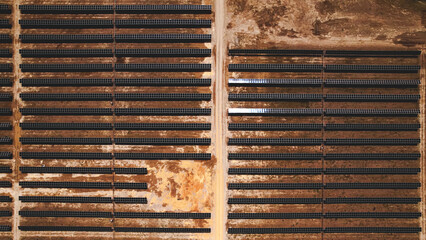 Drone high-angle shot of a vast solar power farm with rows of photovoltaic panels in a dry landscape, illustrating renewable energy and sustainable technology infrastructure.