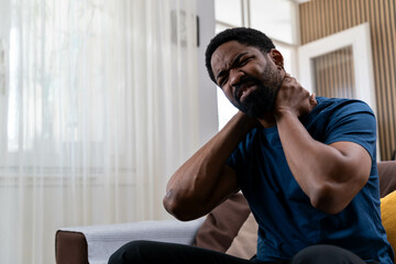 Unhappy man suffering from neck pain at home. Young man feeling exhausted and suffering from neck...