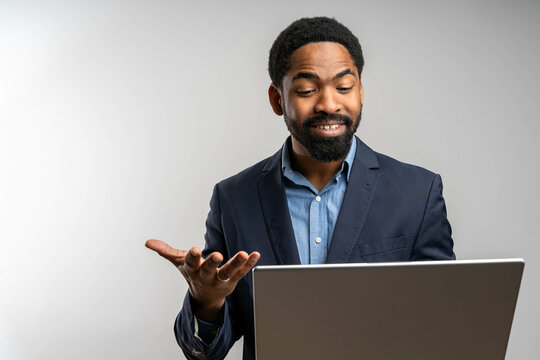 young cheerful black businessman using laptop for video call, smiling and engaged in conversation, standing against bright isolated studio background, professional look.