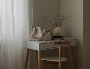 A shopping bag, a laptop, a notebook, a vase with branches on a white table in the living room. Cozy minimalistic interior