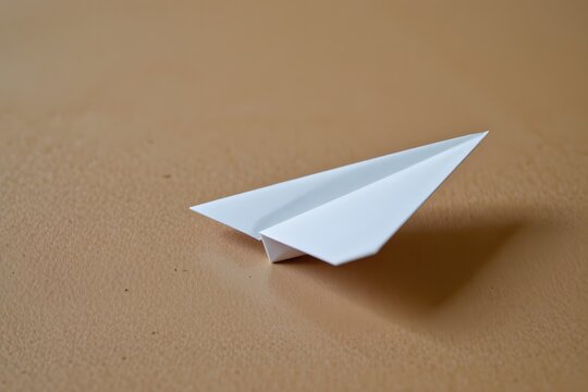 Paper Airplane on Brown Surface: A pristine paper airplane, carefully folded, rests on a smooth, inviting brown surface, symbolizing dreams, journeys, and the simplicity of flight.