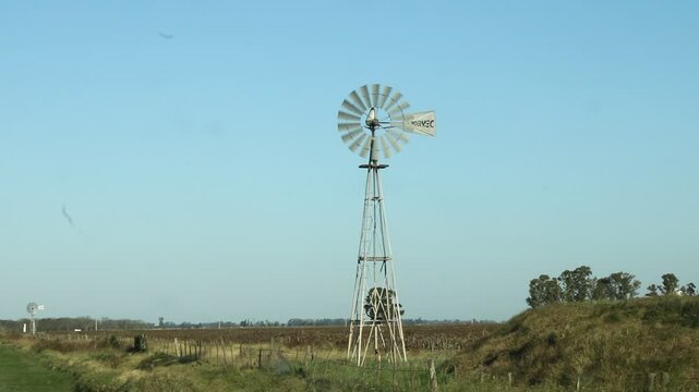 Molino de viento en el campo rural para extracci&oacute;n de agua potable para el ganado vacuno, con el viento acciona una bomba que extrae el agua, un hermoso dise&ntilde;o ecol&oacute;gico y sustentable con cielo azul.