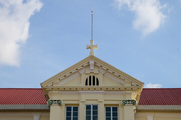 Upper pediment of a colonial era neoclassical architecture style institution building with prominent cross at apex in Taiping, Perak, Malaysia