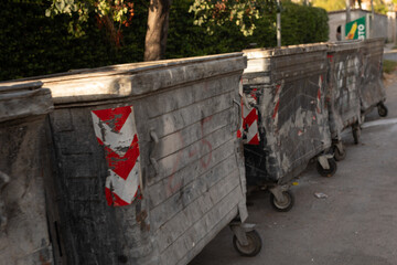 Aged dumpsters line a street, showing wear and faded red & white chevron markings.  Urban decay scene.