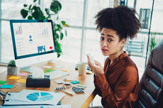 Young businesswoman in an office with modern decor, working while unwell, seated at a desk with computer and papers.
