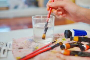 Close-up of a little girl hand holding a paintbrush in a glass of water