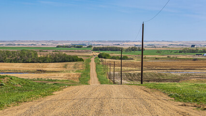 Early Spring Saskatchewan prairie landscape featuring a straight, going down the hill grid road...