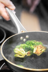 Freshly sautéed broccoli in a frying pan with steam rising, held by a hand. High-heat cooking creates a slightly charred, vibrant green texture