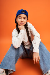 Stylish teenage girl poses in trendy outfit against vibrant orange backdrop