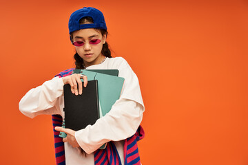 Stylish teenage girl showcasing confidence in vibrant studio on orange background