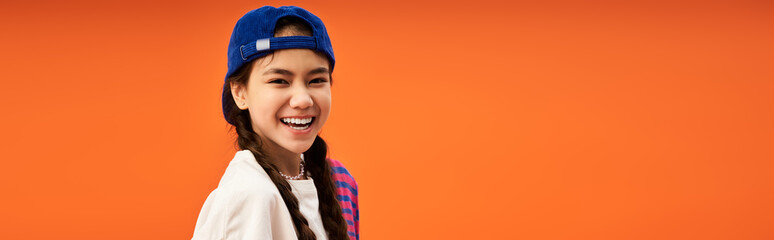 Stylish teenage girl posing confidently in studio with vibrant orange backdrop