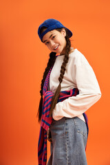 Stylish teenage girl poses confidently in vibrant studio setting with orange backdrop