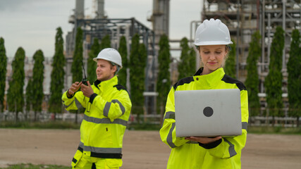 caucasian white engineers in safety uniforms and helmets using laptop and radio for site communication. Concept of teamwork, inspection, and operations at an industrial facility.Construction of Oil, 