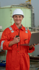 caucasian white engineers in safety uniforms and helmets using laptop and radio for site communication. Concept of teamwork, inspection, and operations at an industrial facility.Construction of Oil, 