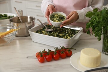 Woman making spinach lasagna at marble table indoors, closeup