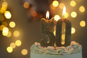 50th birthday. Burning number shaped candles on cake against blurred background with lights, closeup and space for text. Bokeh effect
