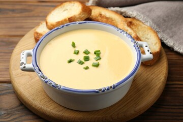 Tasty cheese dipping sauce in bowl and croutons on wooden table, closeup