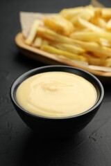 Tasty cheese sauce in bowl and French fries on black table, closeup