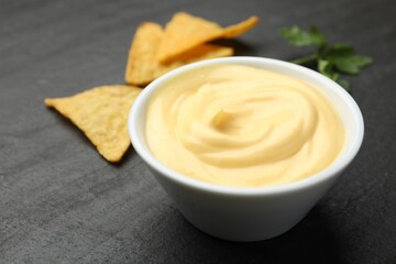 Tasty dipping cheese sauce in bowl, nacho chips and parsley on black table, closeup. Space for text