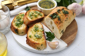 Tasty bread with garlic, herbs and oil on white tiled table, closeup