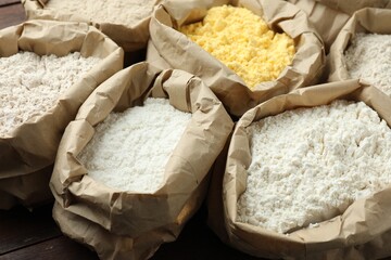 Different types of flour in paper bags on wooden table, closeup