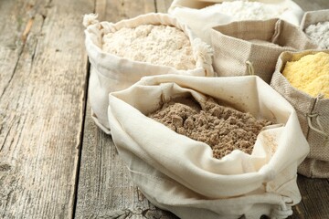 Different types of flour in bags on wooden table, closeup. Space for text