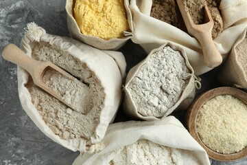 Different types of flour in bags on grey textured table, flat lay