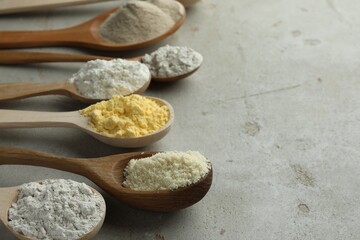 Different types of flour in spoons on light grey table, closeup. Space for text
