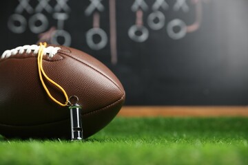 American football ball and whistle on green grass against chalkboard with game scheme, closeup....