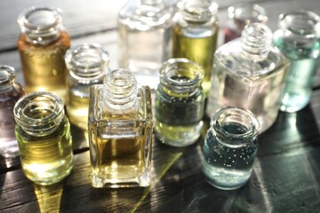 Perfume bottles with aromatic oils on black wooden background, closeup