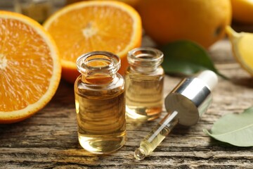 Open perfume bottles with aromatic essential oils, pipette, oranges and leaves on wooden table, closeup