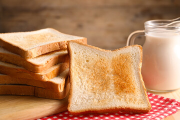 Slices of tasty toasted bread and jug of milk on wooden table, closeup