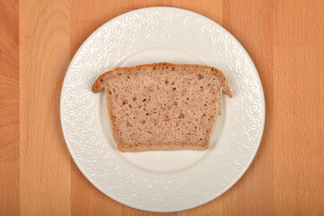 Slice of breadA single slice of light brown, porous bread rests on a white, patterned plate set against a light brown wooden surface