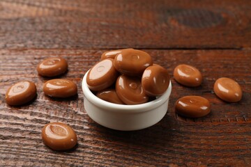 Many tasty caramel candies on wooden table, closeup