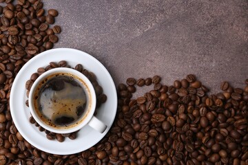 Aromatic coffee in cup, saucer and beans on brown textured table, flat lay. Space for text