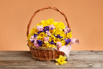 Wicker basket with beautiful flowers on wooden table against coral background