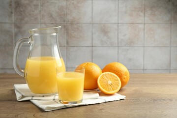 Fresh orange juice and fruits on wooden table against grey tiled wall